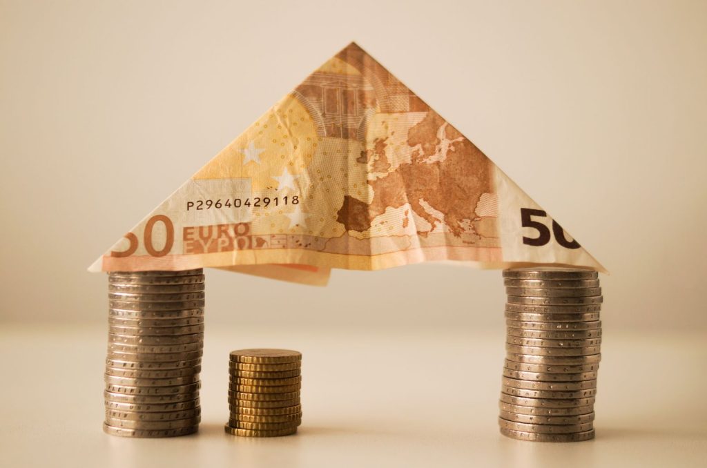 Euro bankbiljet gevouwen als dak op stapels munten, symbool voor financiering van een woning